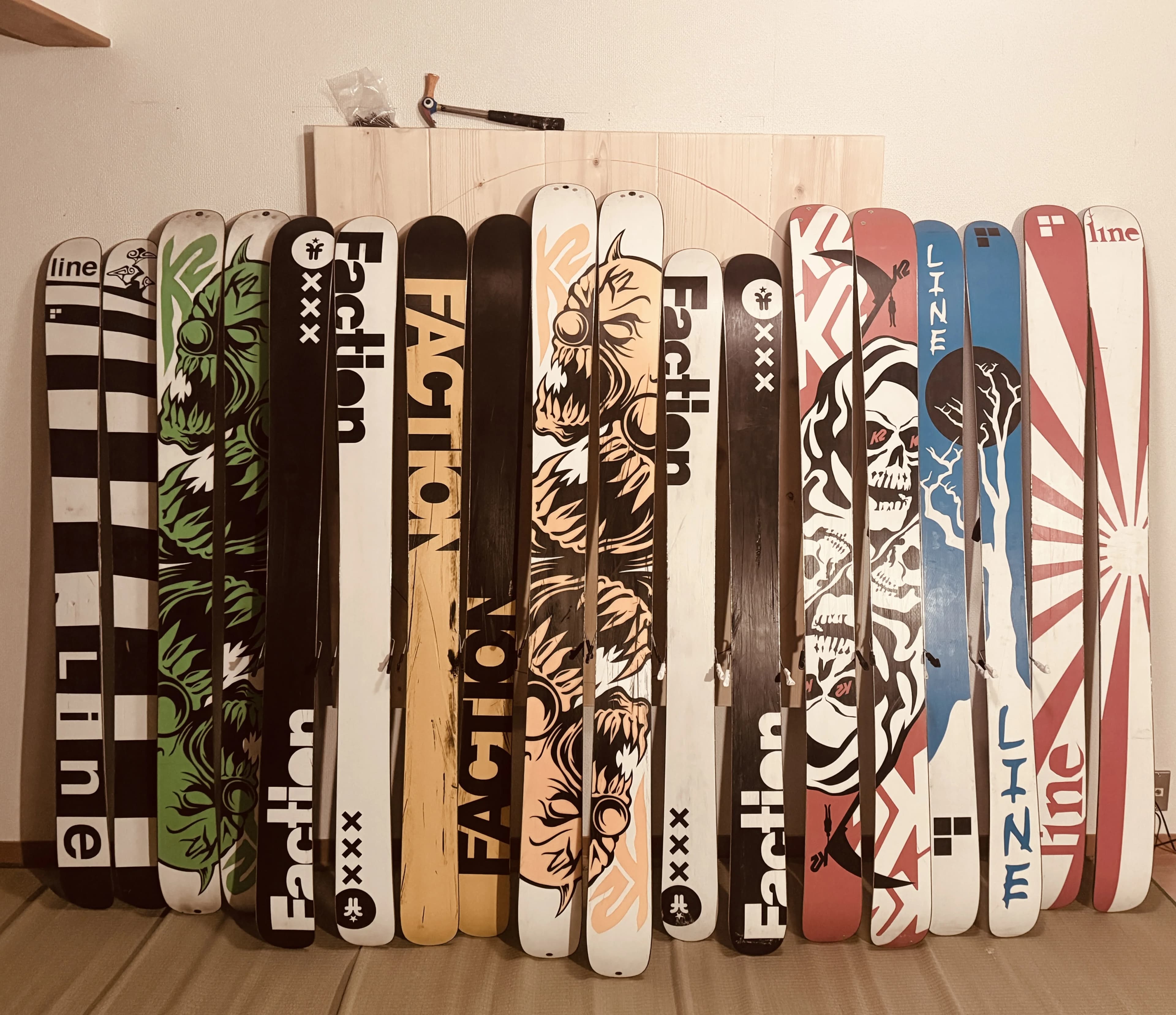 A collection of powder skis arranged against a wall, including K2 Hellbents, Faction Royales, Line EP Pros, and Line Bacons