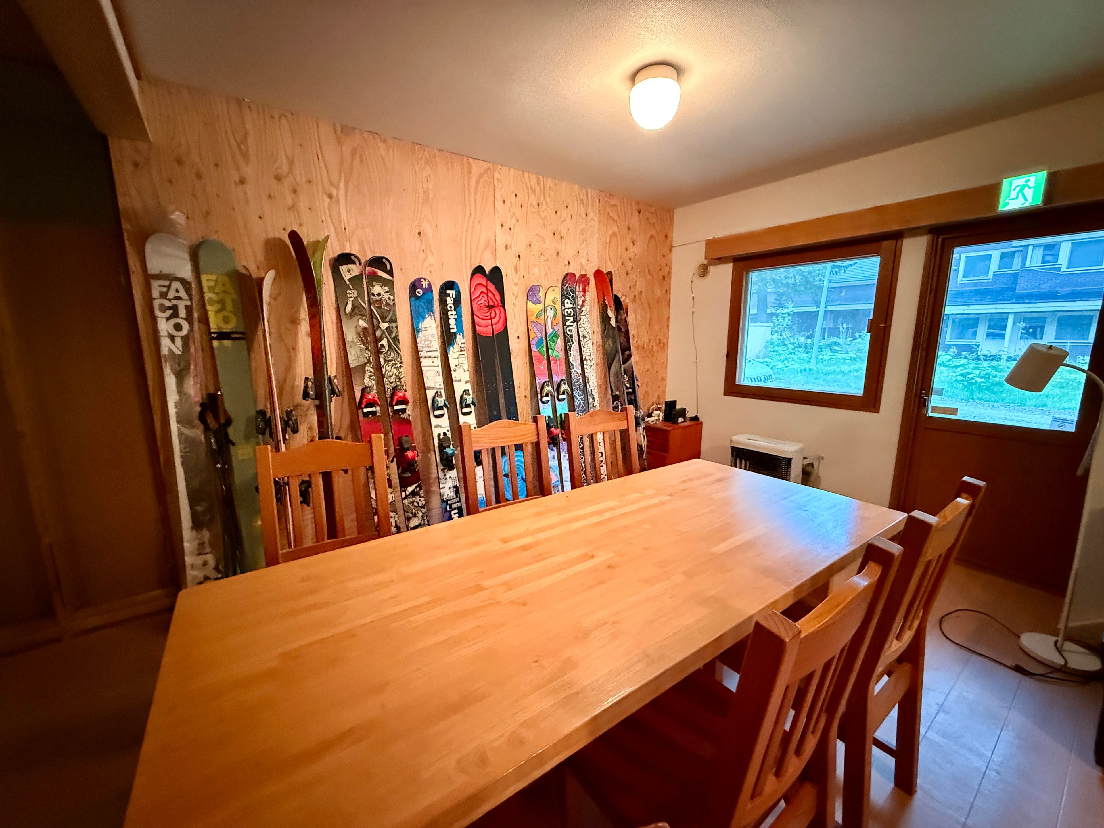 Shared living room at Wakaranai Lodge with a long table and powder skis leaning against a plywood wall