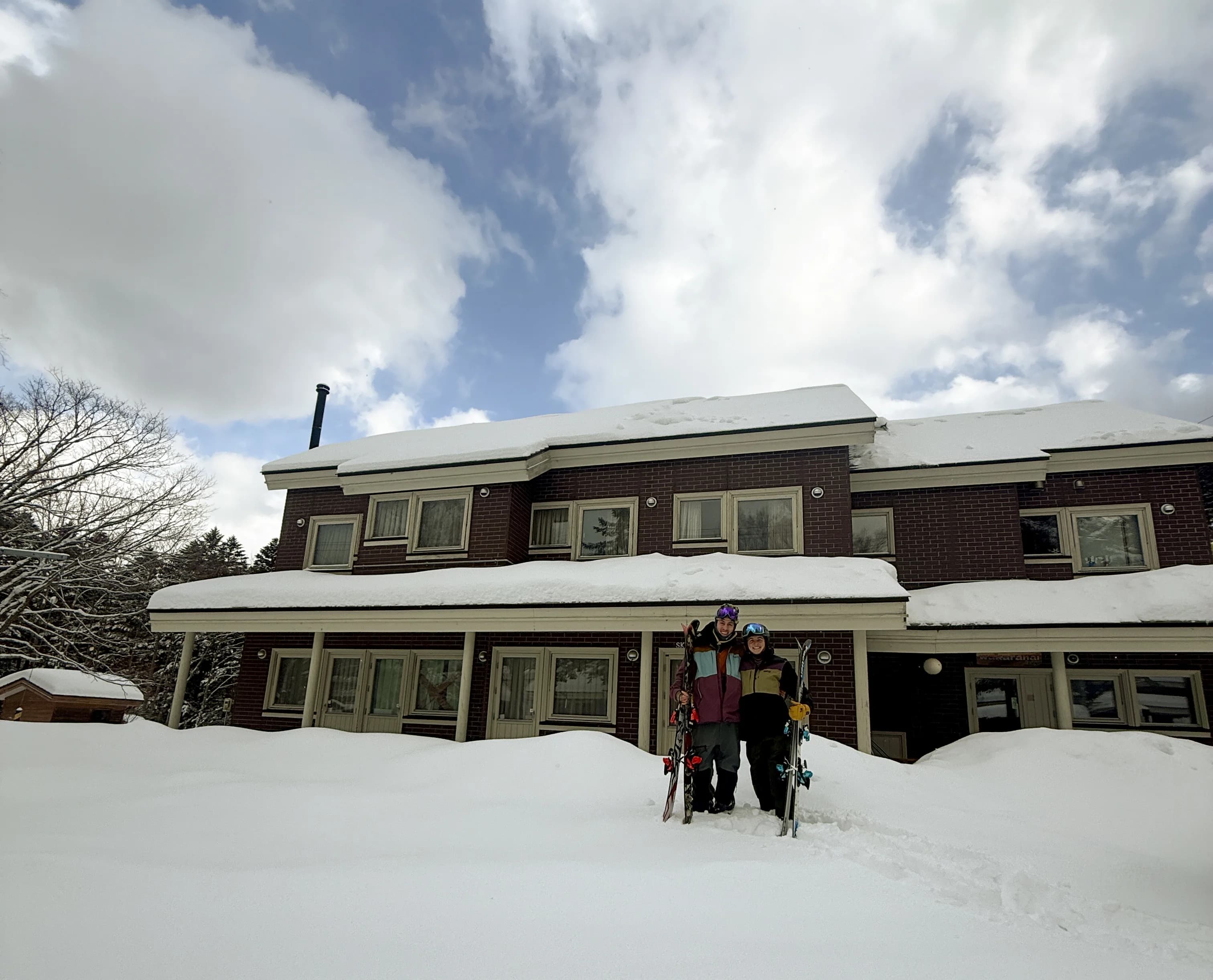 Riley and Denise standing in front of Wakaranai Lodge in winter with skis